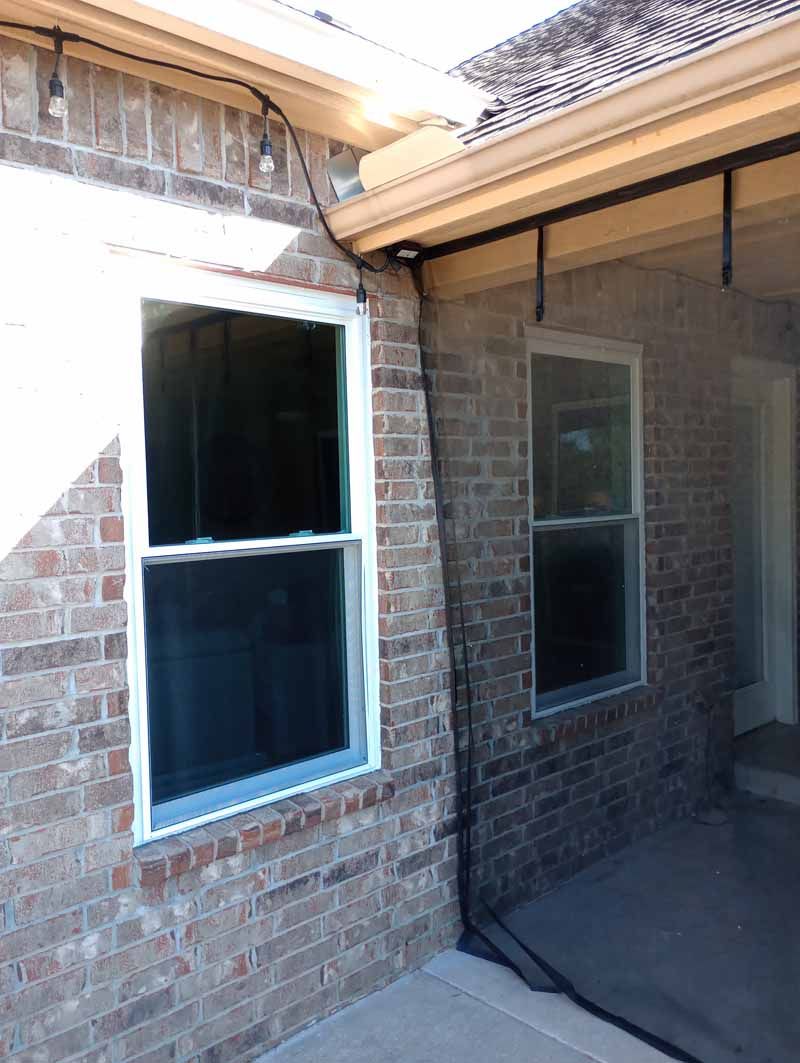 Exterior view of a brick house with two white-framed windows and an awning over a small patio area.