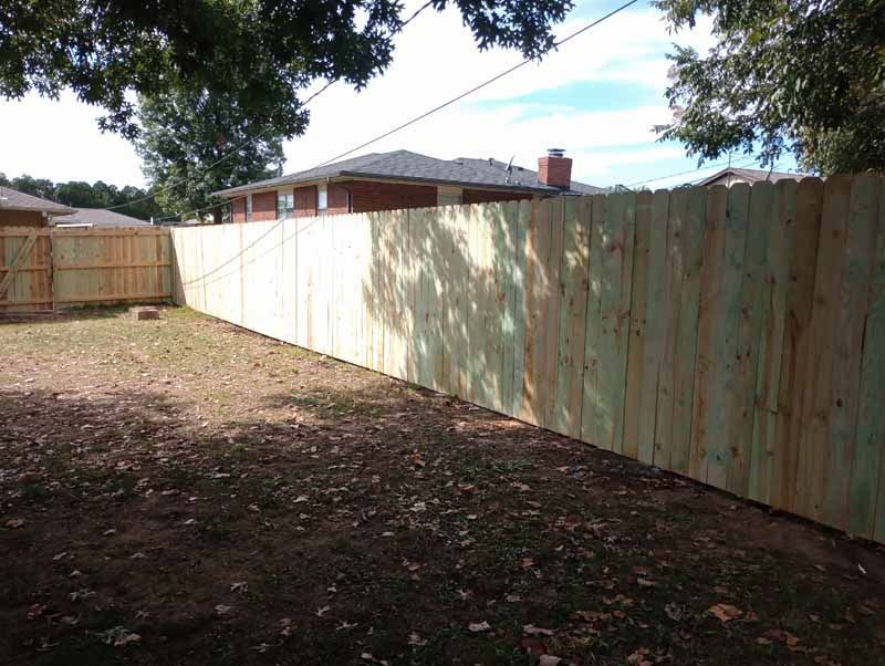 Wooden privacy fence in a backyard, with lawn, trees, and houses in the background.