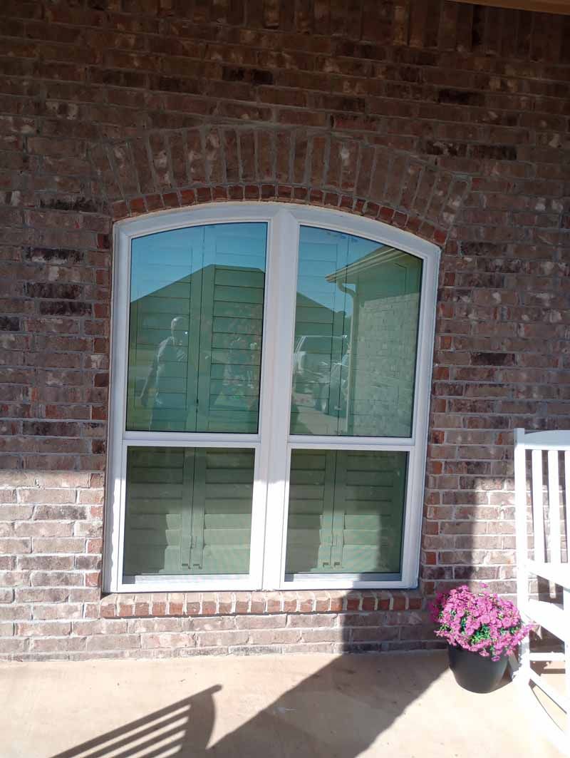 White-framed window with arched top set in a brick wall. Reflections visible in the glass.
