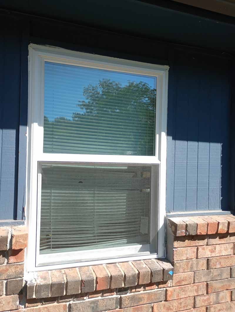White-framed window with blinds, set against a dark blue wall above a brick exterior.