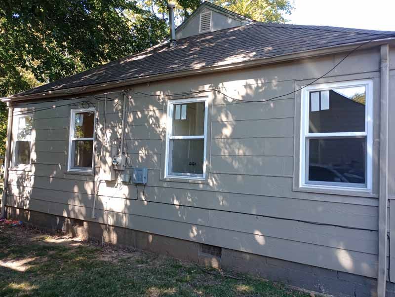 Exterior of a house with new white-framed windows, tan siding, and a brown roof.