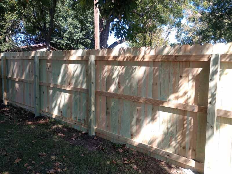 Wooden fence in a yard, green grass, and trees in background.