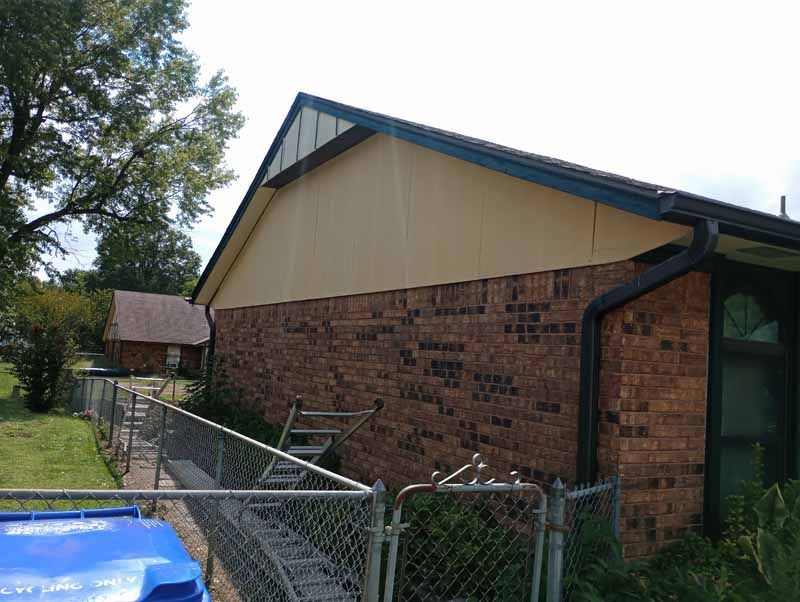 Brick building with tan siding, black gutter, and chain-link fence.