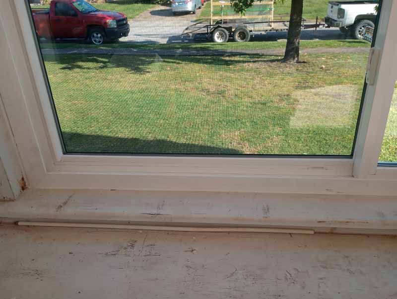 View through a window, looking out to a yard, a red truck, and a trailer.
