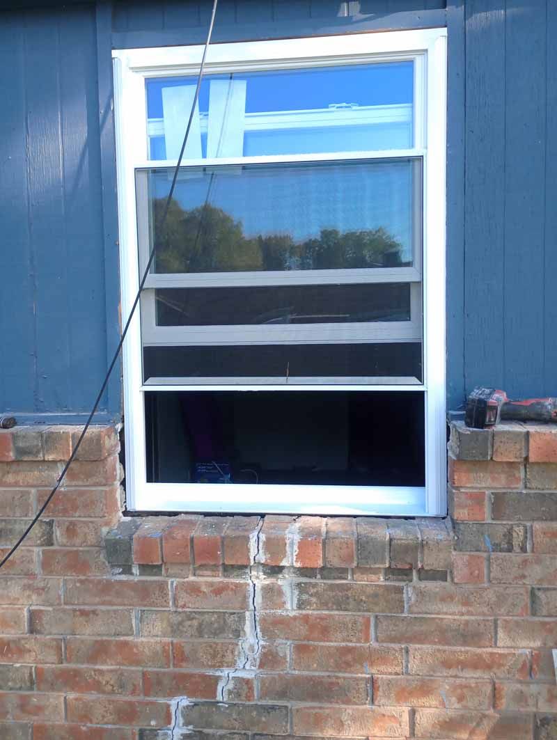 Window, partly open, in a blue wall, set on a brick foundation.