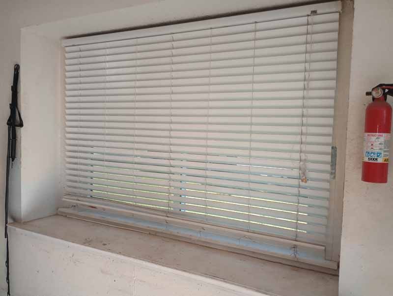 Window with closed white blinds, window sill, fire extinguisher to the right.