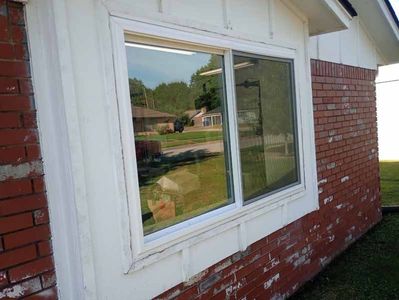White-framed sliding window on a brick building reflects a residential street with trees and vehicles.