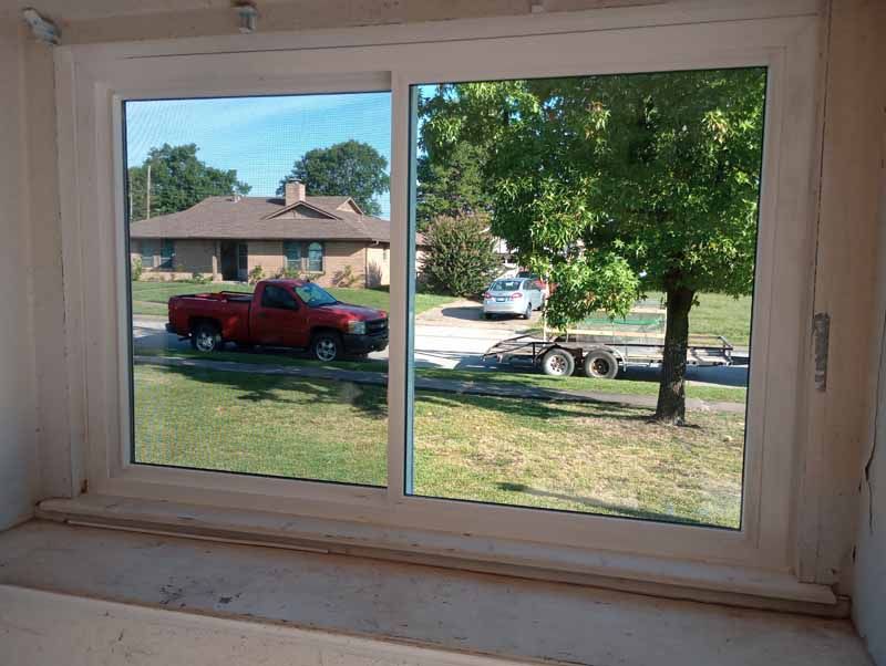 Window view of a red pickup truck and trailer on a sunny residential street.