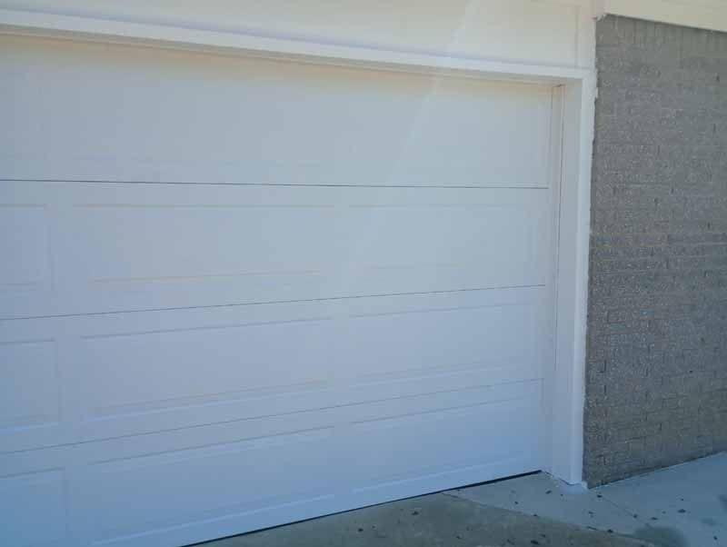 White garage door with white trim, set against a concrete wall and driveway.