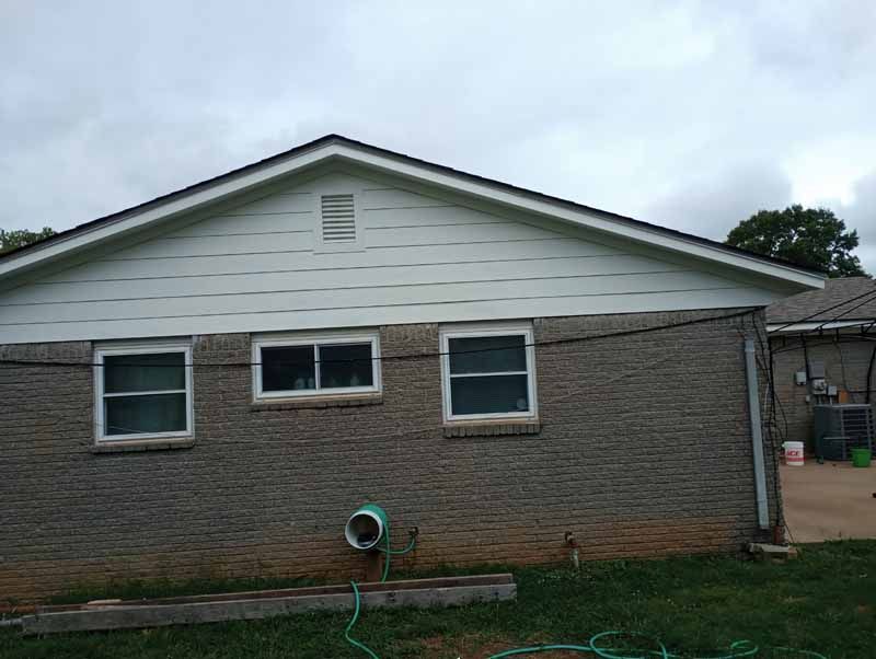 Brick house exterior with three windows, white siding, and a dark roof under a cloudy sky.
