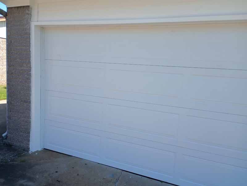 White garage door on a concrete driveway, next to a brick wall.