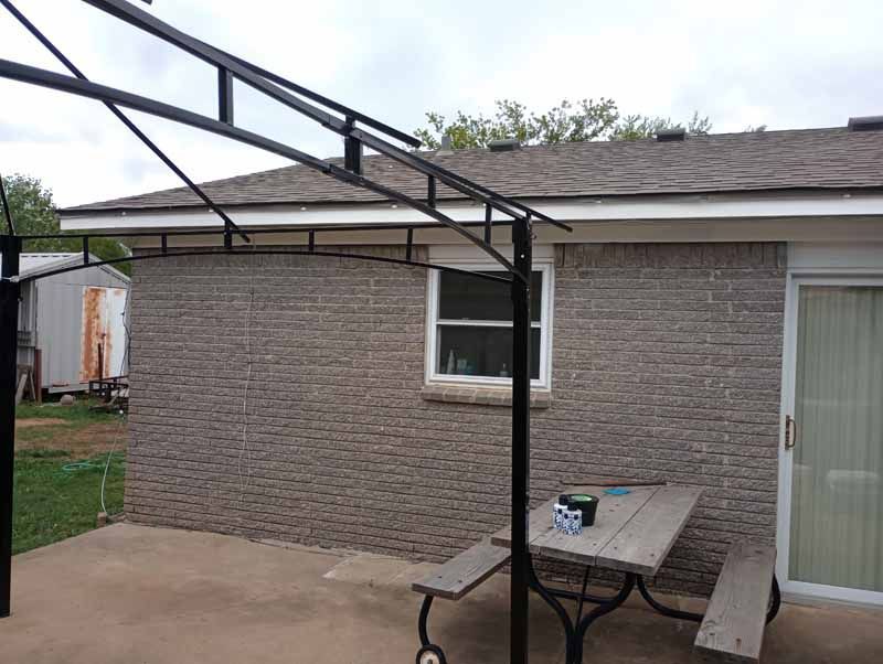 Outdoor patio with a brick wall, window, picnic table, and black metal structure.