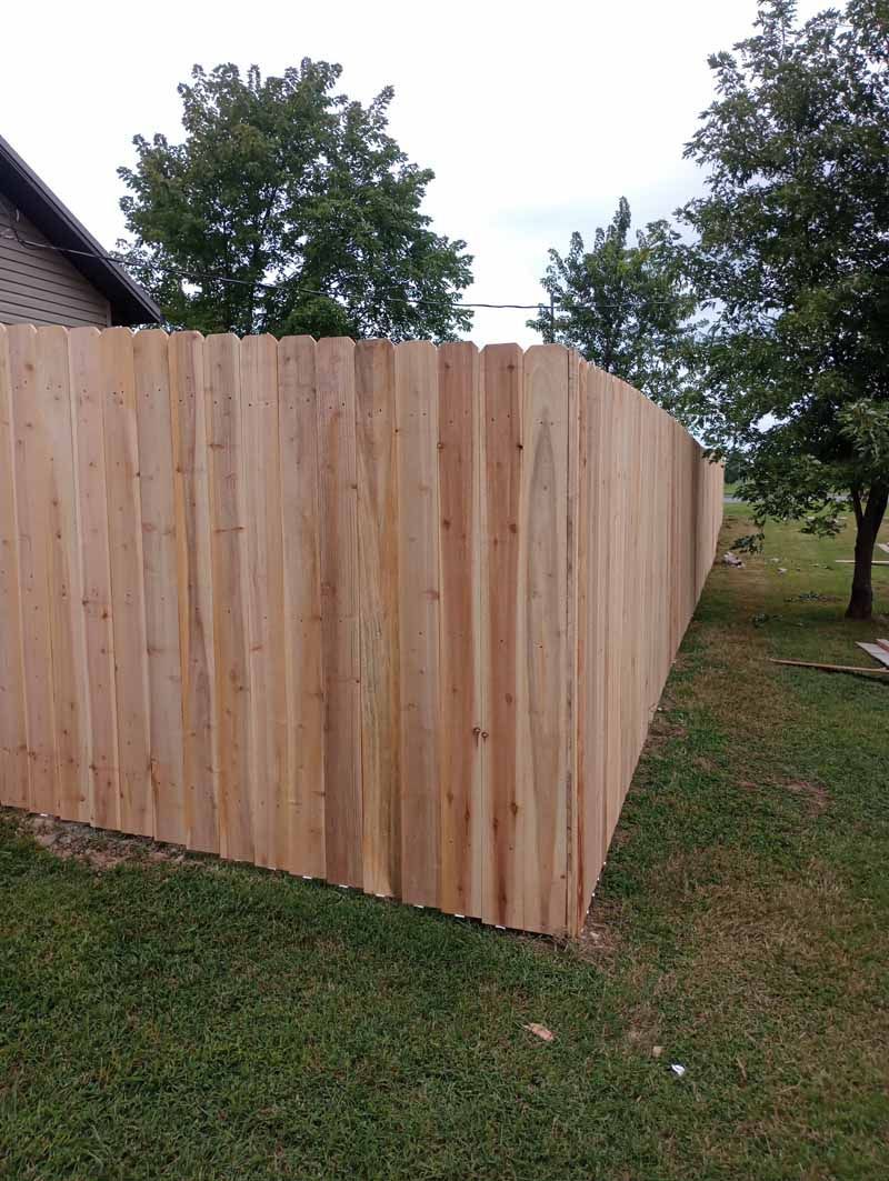 Wooden privacy fence in a grassy yard, under cloudy sky, trees in the background.