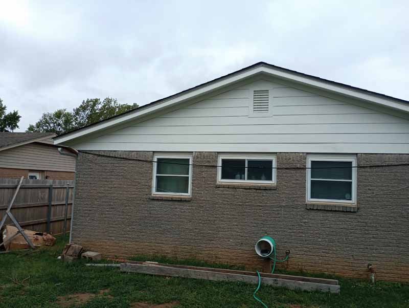 Brick house exterior with three windows, white trim, and a dark roof under a cloudy sky.