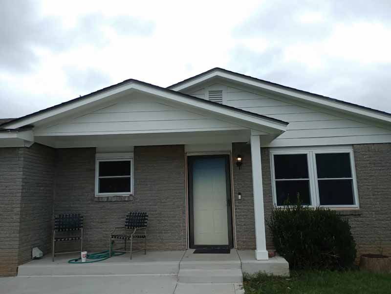 A brick house with a porch and two chairs, overcast sky.