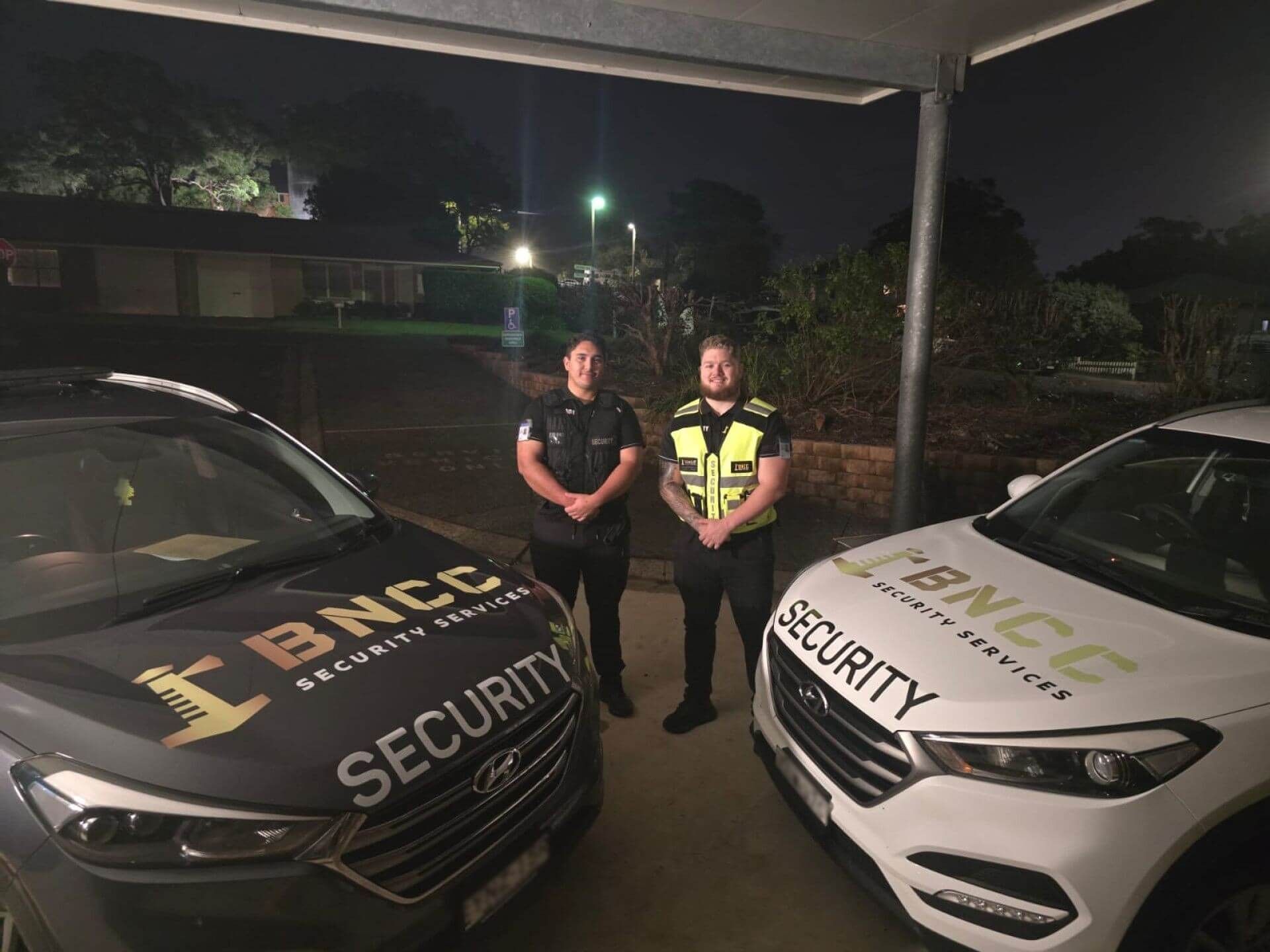A White and Black patrol car with the two security guards outside the cars— BNCC Security Services in Port Macquarie, NSW