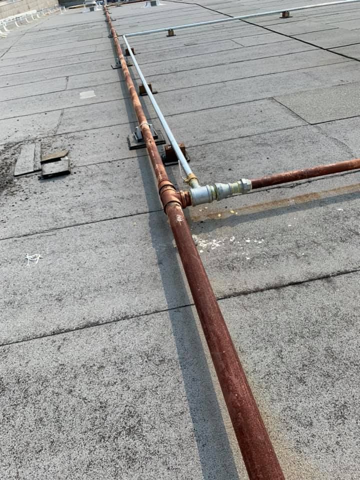 A row of rusty pipes are connected to a roof.