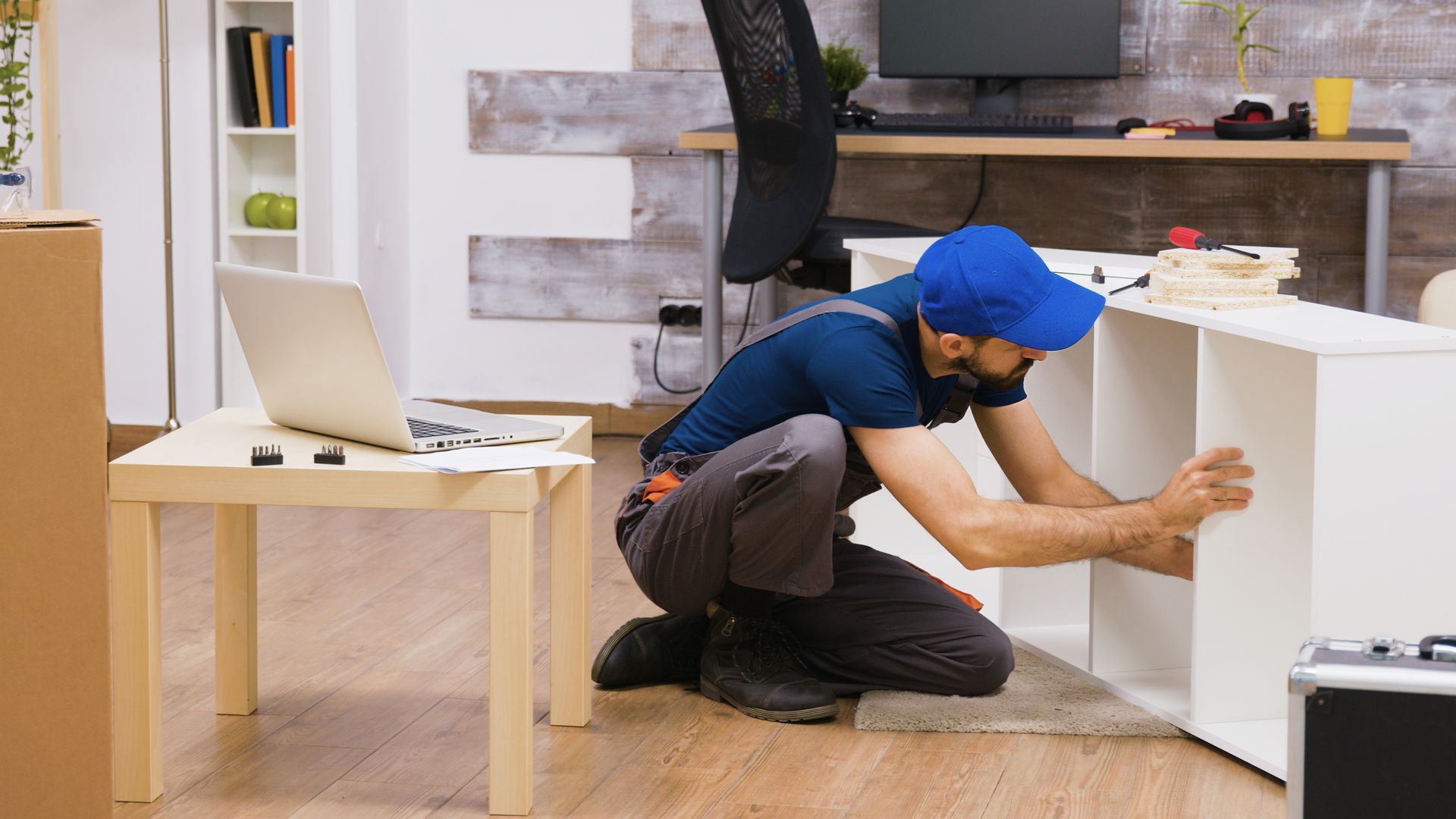 a man is kneeling down to install a bookshelf in a living room .
