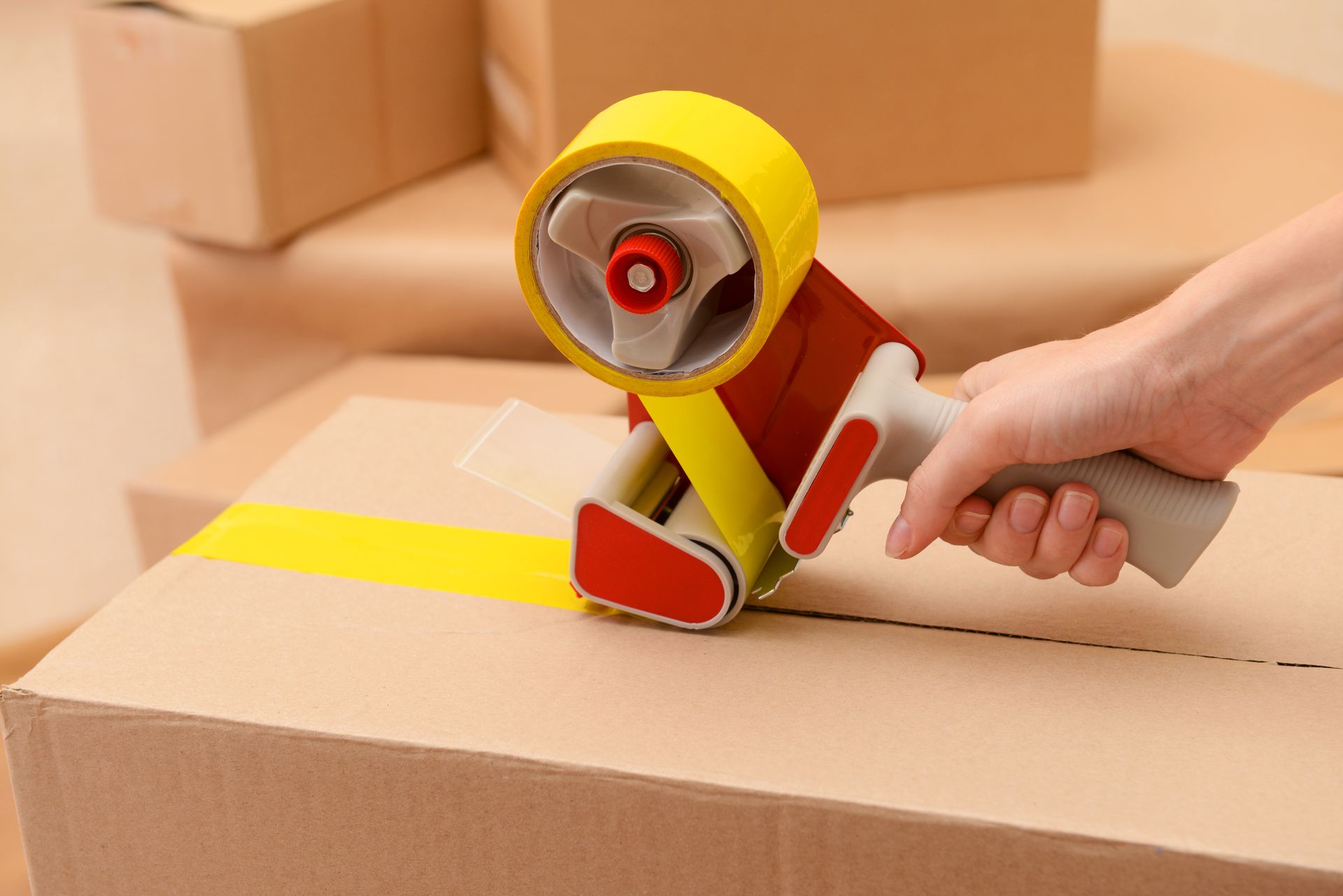 a person is using a tape dispenser to seal a cardboard box .