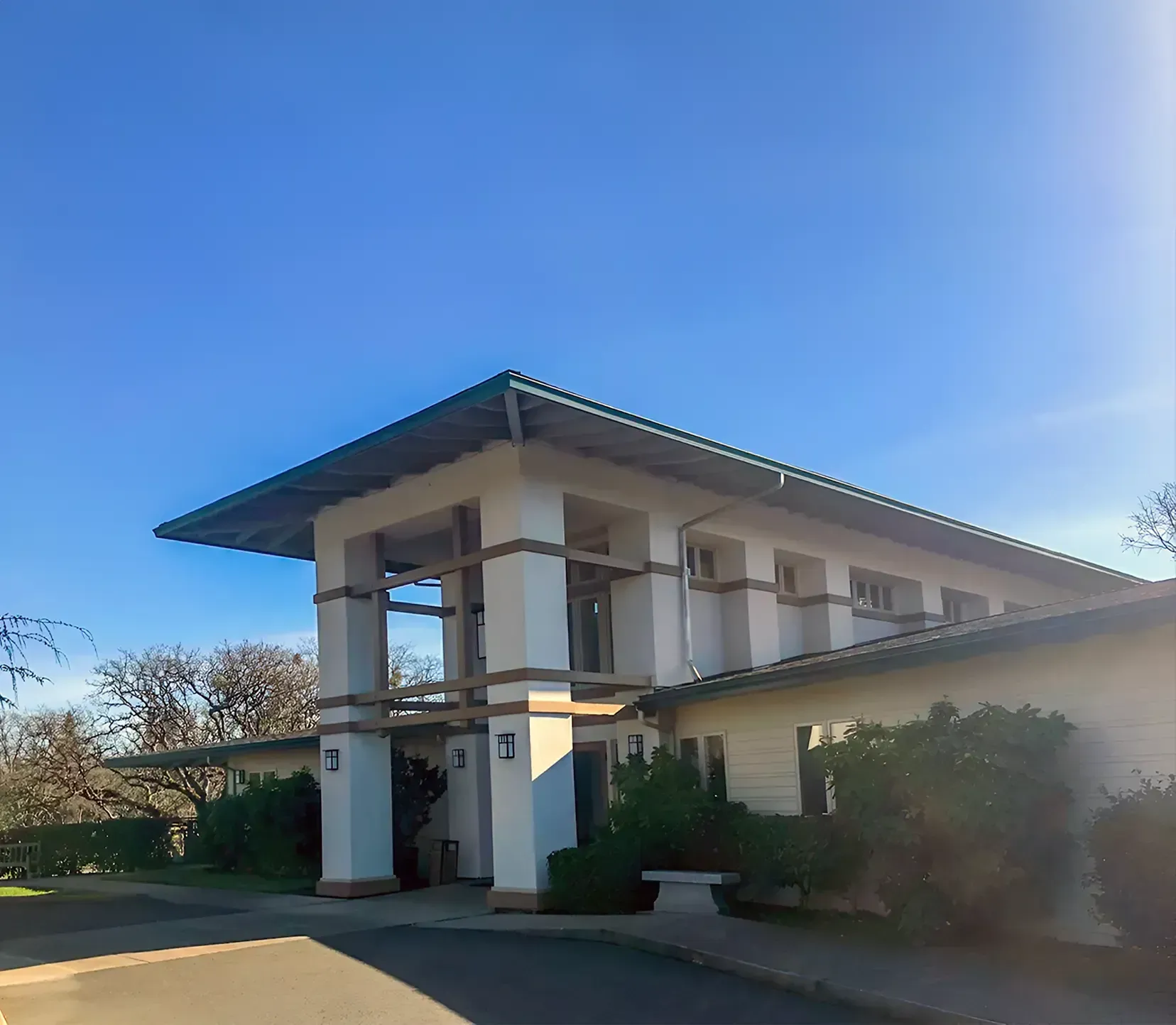A light-colored building with a flat roof, large pillars, and a clear blue sky.