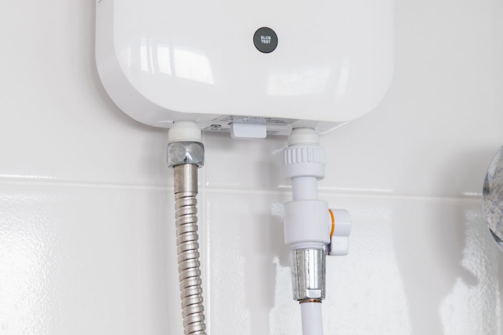 White Electric Water Heater with Connected Metal and Plastic Pipes on A Tiled Wall — Lakeside Gas Fridges In Argenton, NSW