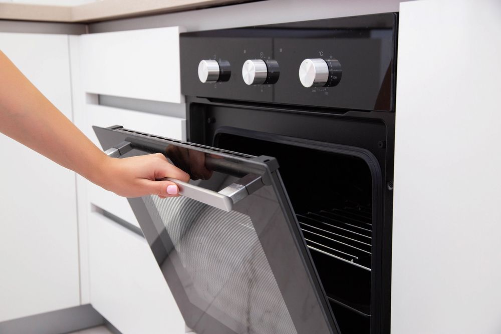 Hand Opening a Black Oven Door in A Modern White Kitchen — Lakeside Gas Fridges In Cessnock, NSW