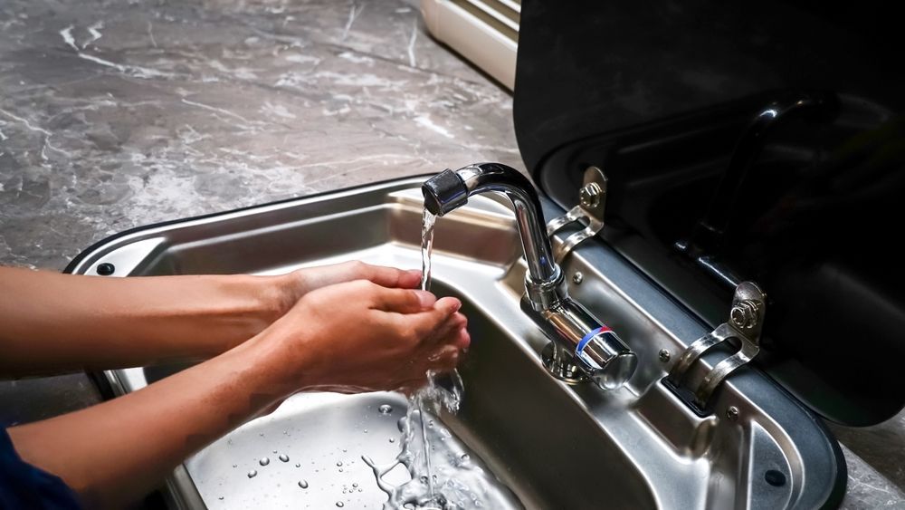 Person Washing Hands in A Stainless Steel Sink, Water Running from A Chrome Faucet — Lakeside Gas Fridges In Argenton, NSW