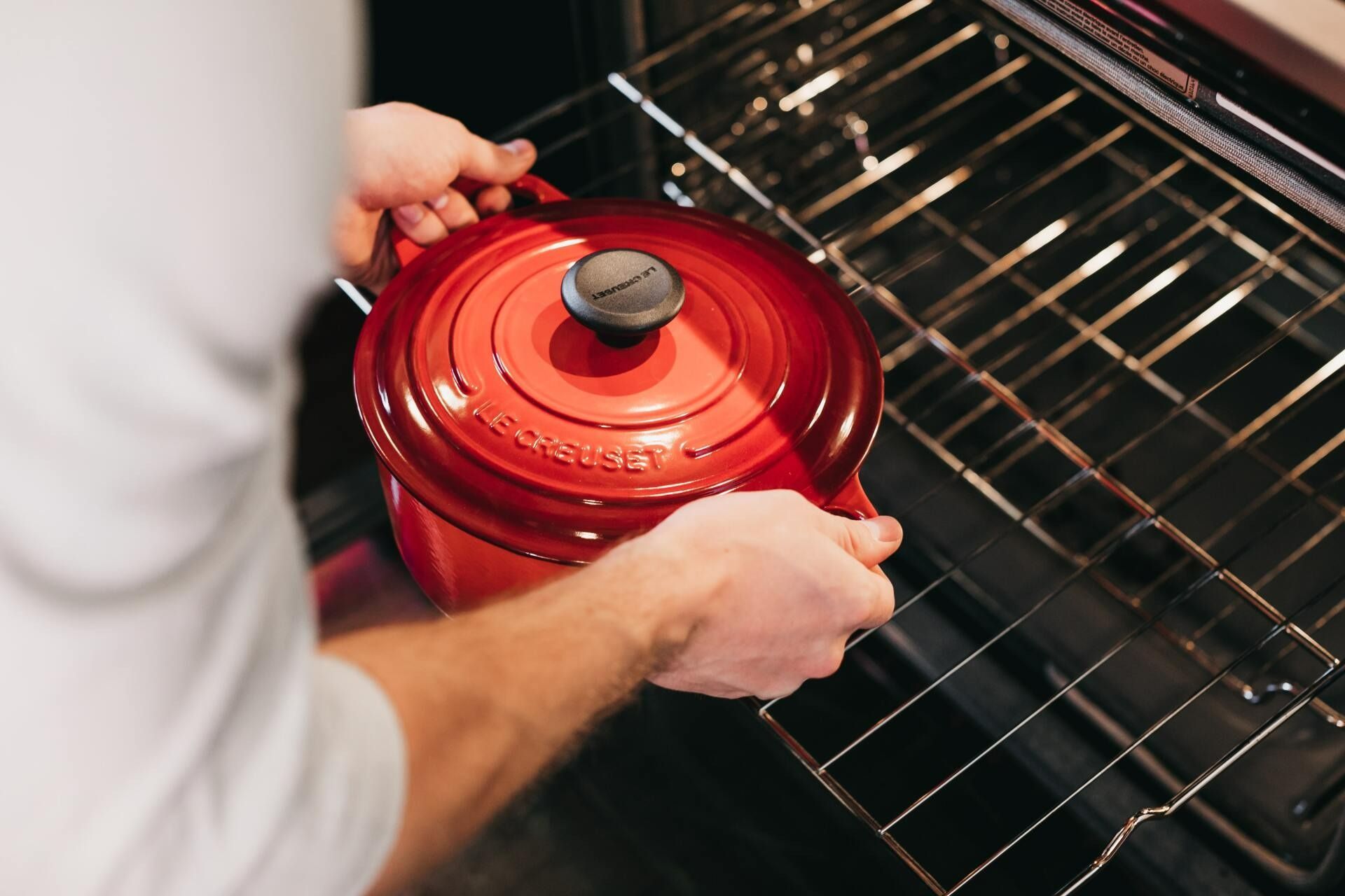 Person Placing a Red Pot Into a Hot Oven, Hands Visible — Lakeside Gas Fridges In Argenton, NSW