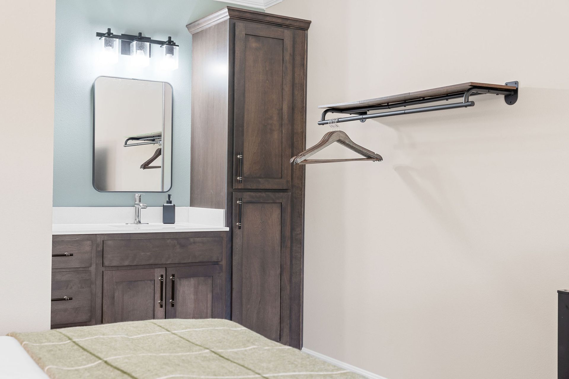 A bedroom with a bathroom , sink , mirror and clothes rack.