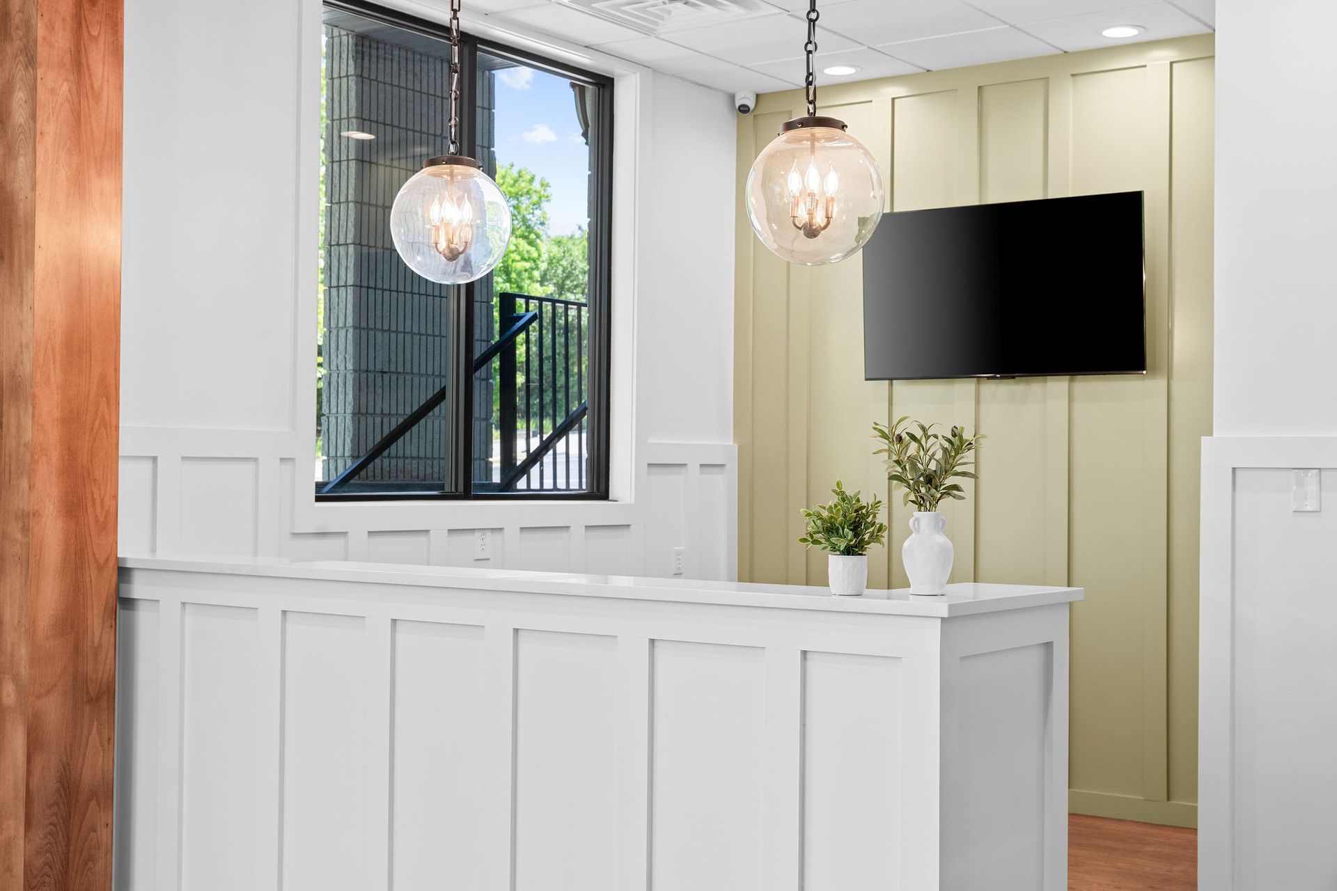 A reception area with a white counter , a television and a window.