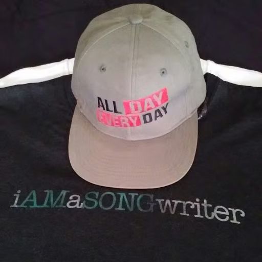 Gray cap with pink “ALL DAY EVERY DAY” text on a black iAmA.songwriter shirt.