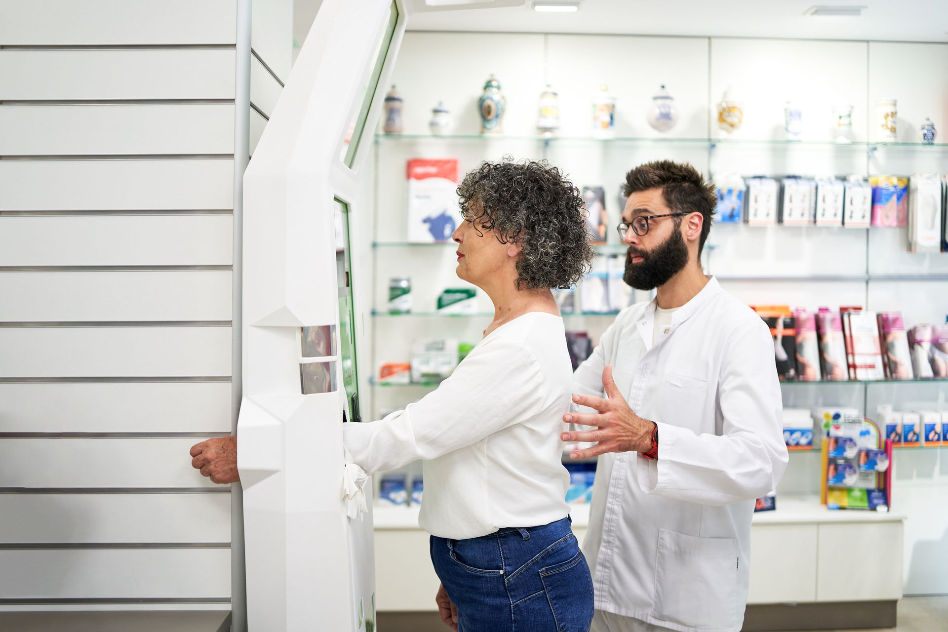 Woman using health machine for medical weight loss services with pharmacist assisting in pharmacy.