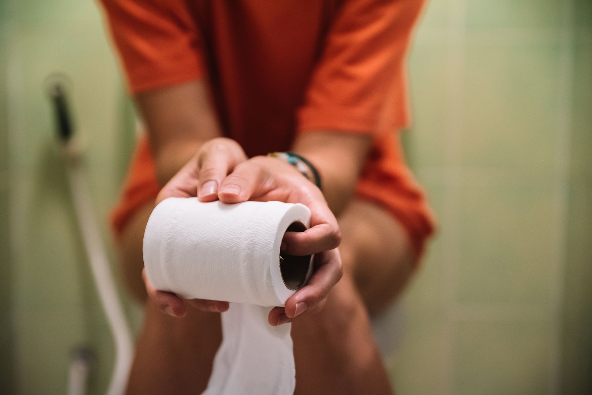 Person sitting on a toilet, holding a roll of toilet paper in their hands.