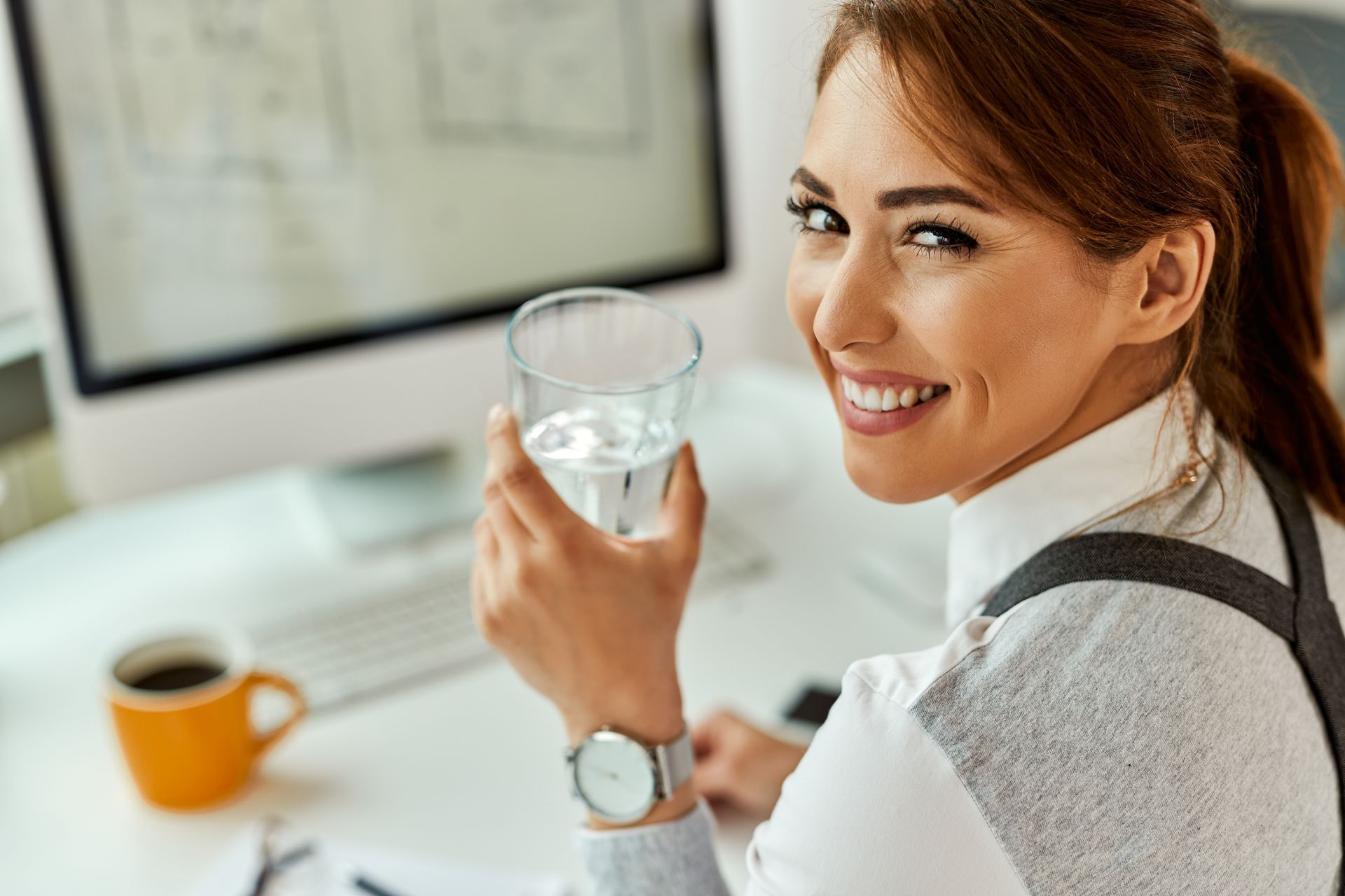 a woman is sitting at a desk drinking a glass of water .