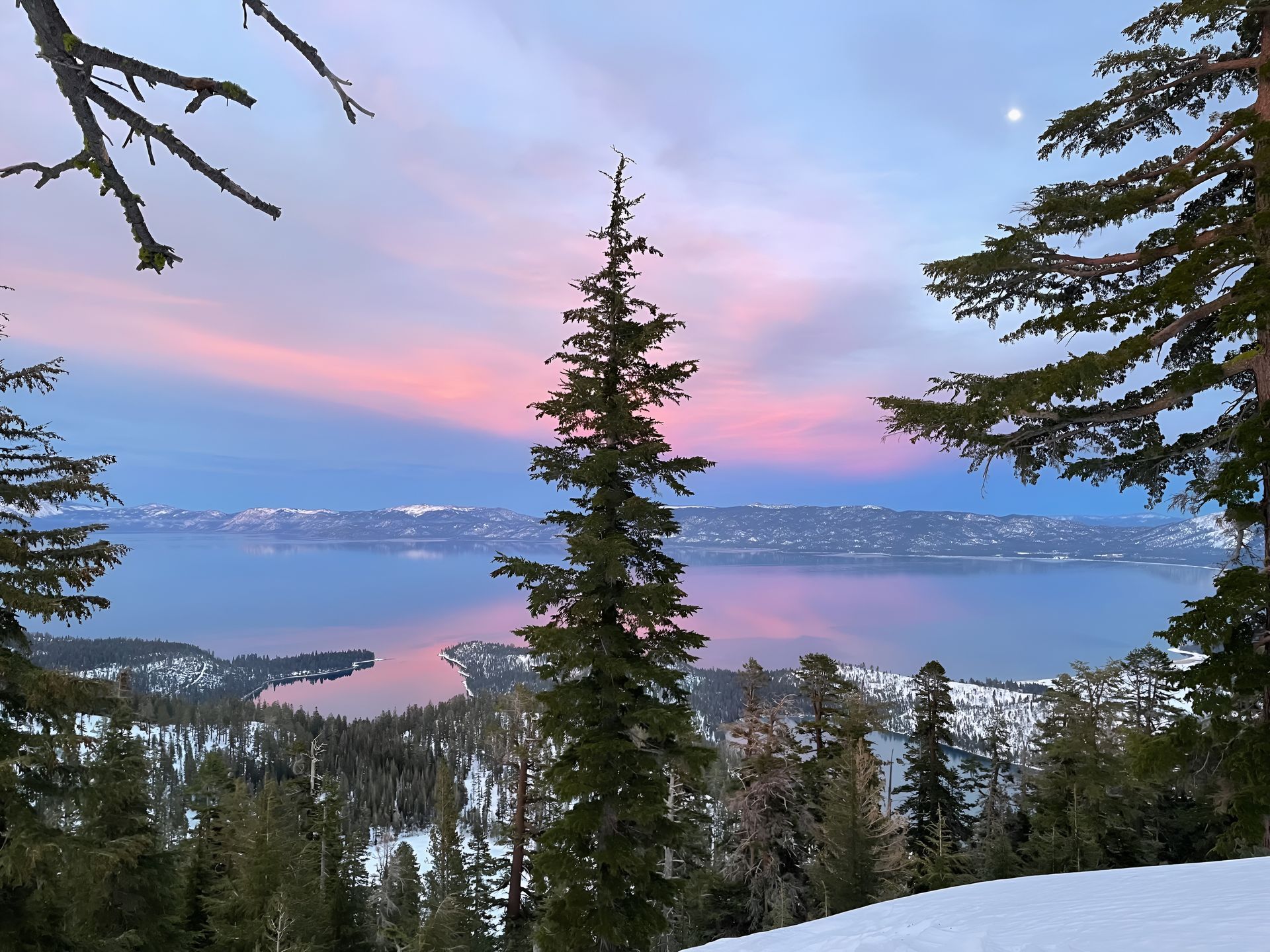 Snowy mountain landscape with a lake reflecting pink and blue sky at sunset.