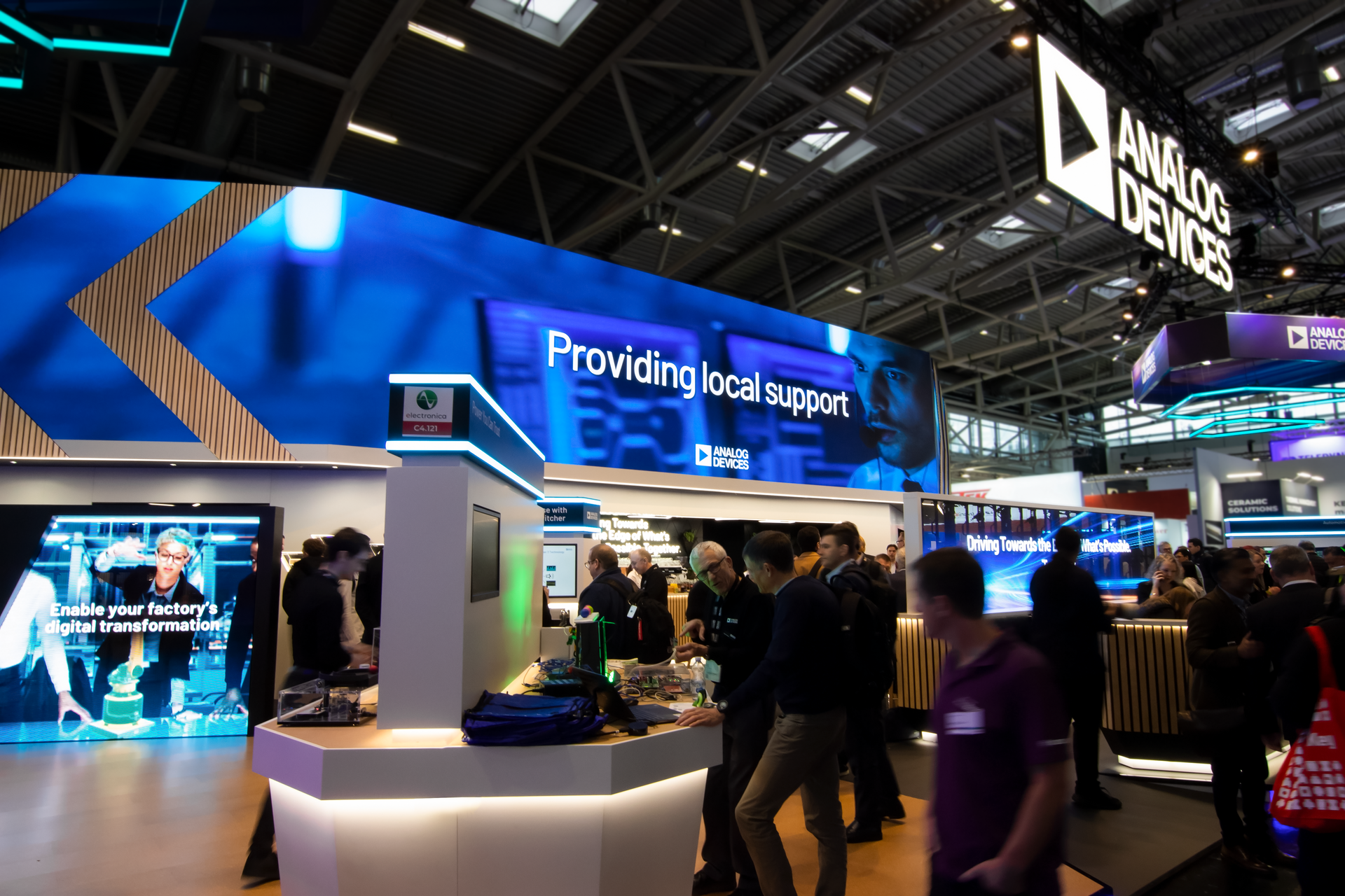 The Analog Devices booth at Electronica 2024, featuring an LED wall, cork flooring and product demonstration areas. 