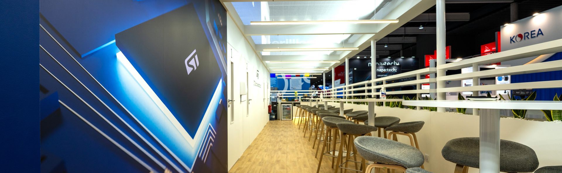 A modern hallway with bar stools, tables, and a large display with blue accents.