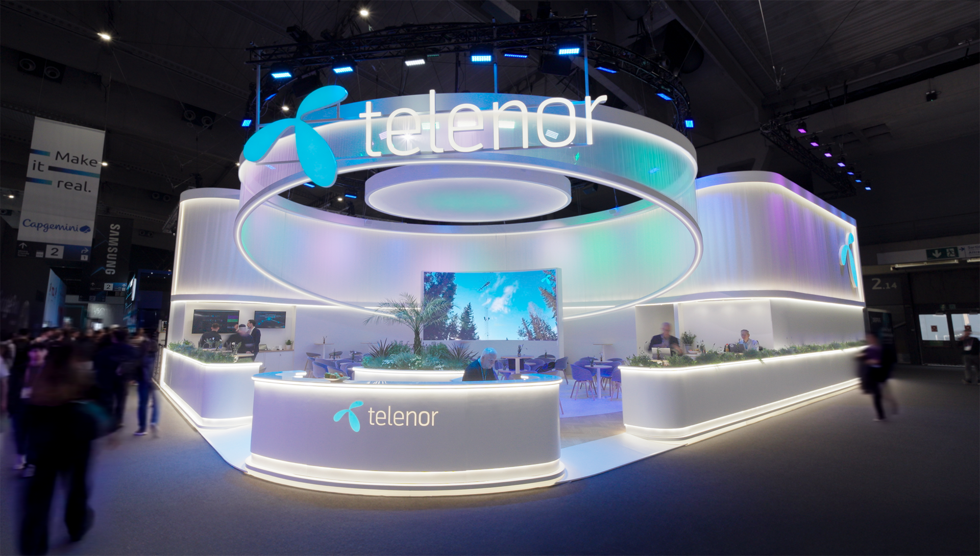 Telenor Group booth at an event; features curved white structure, blue screens, logo, and plants.