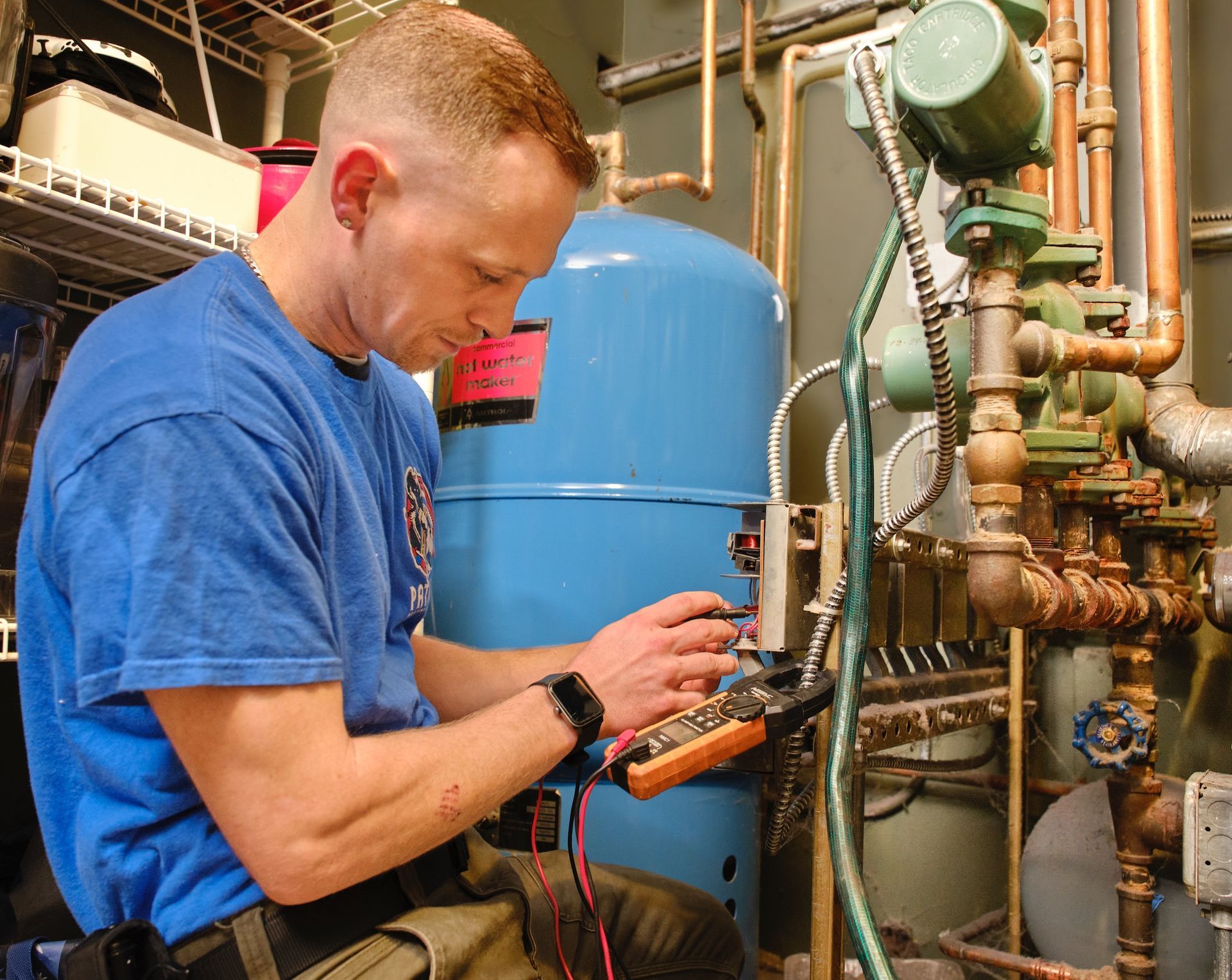 Electrician in yellow hard hat working on wiring inside a wall.