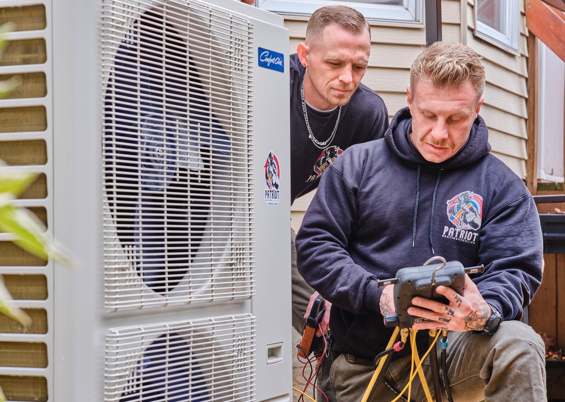 Electrician in yellow hard hat, overalls, black gloves works on electrical panel. Window in background.