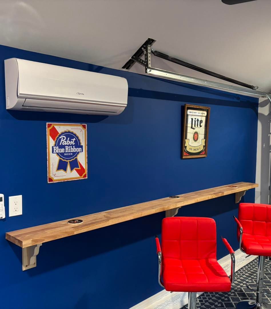 A bar area with blue wall, wooden shelf, red bar stools, and beer signs. An air conditioner is mounted above.