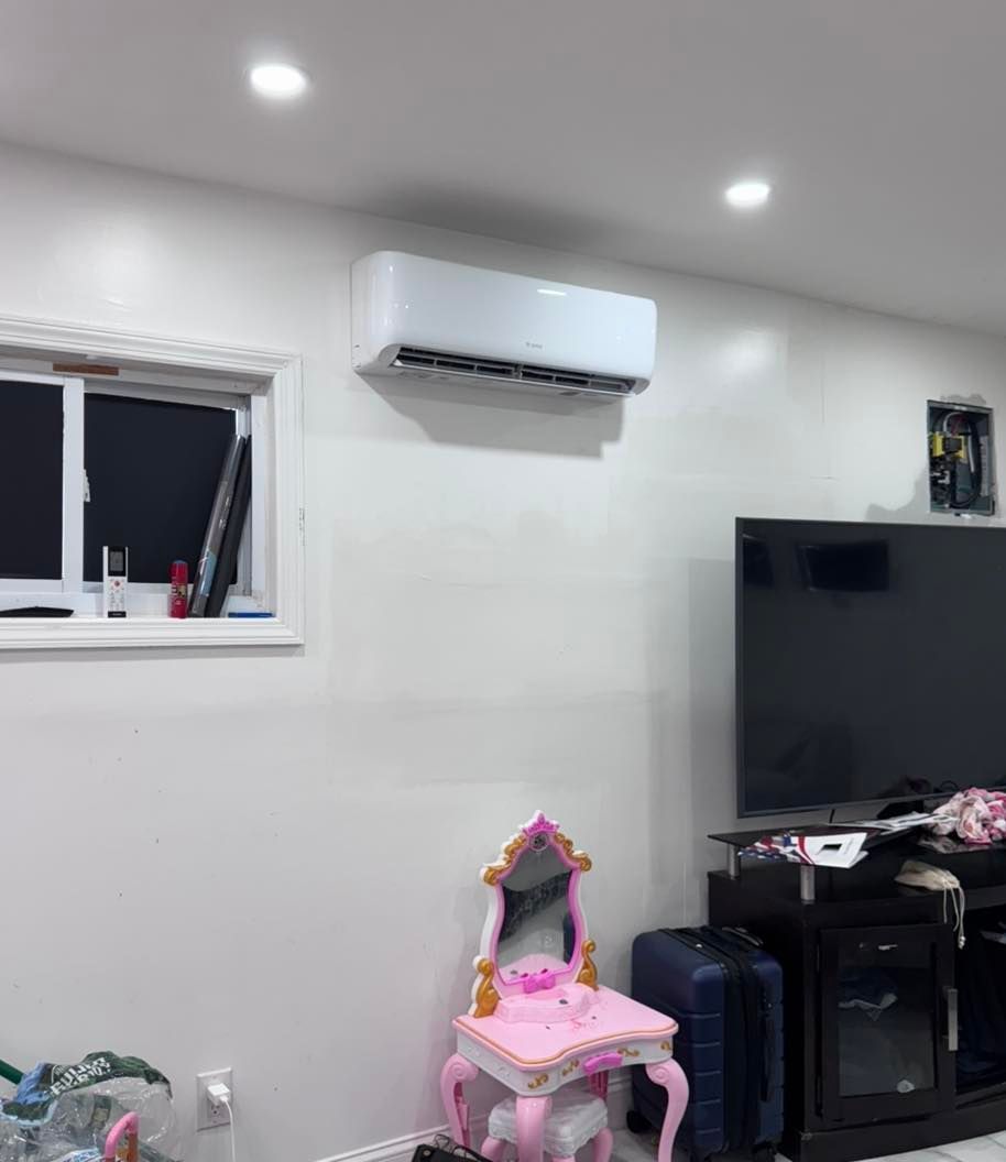 White wall-mounted air conditioner in a living room; a small vanity and TV are also visible.