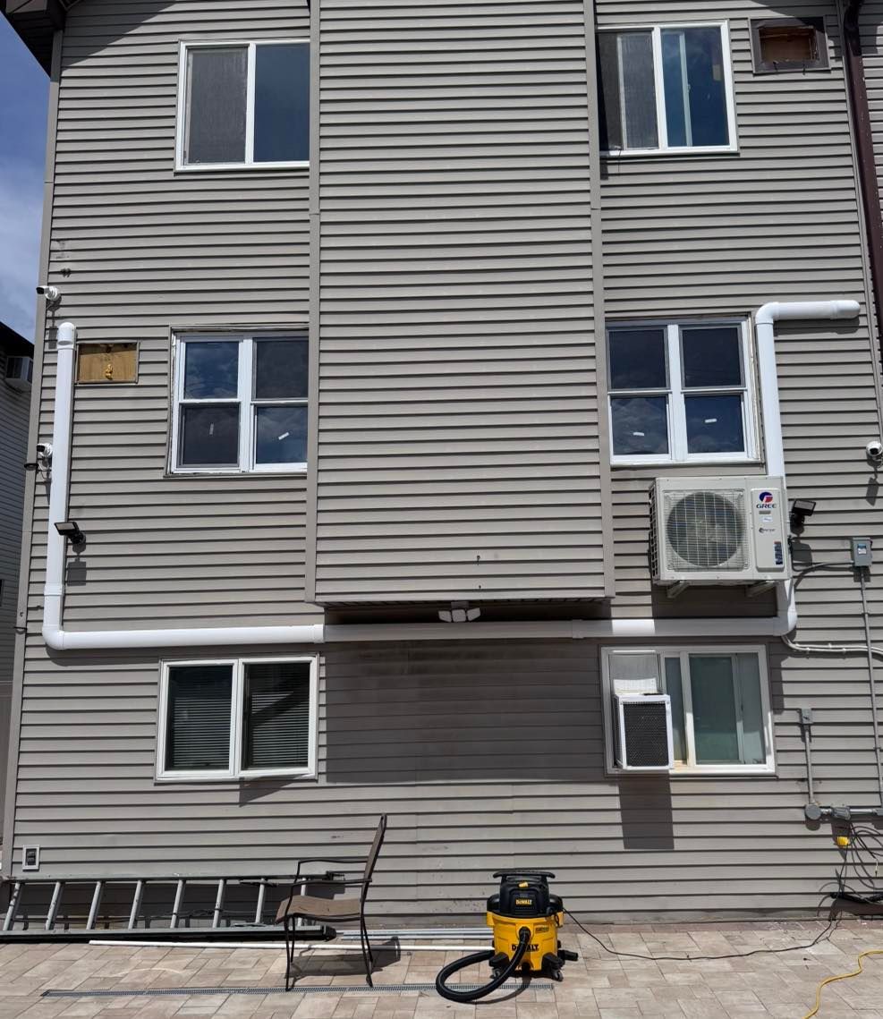 Gray building with several windows, an AC unit, and white pipes on the exterior.