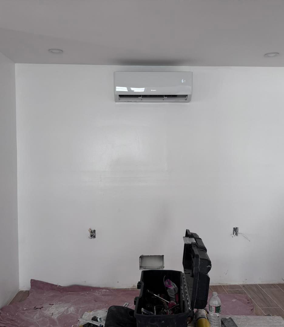 Air conditioning unit mounted on a white wall in a room under construction.