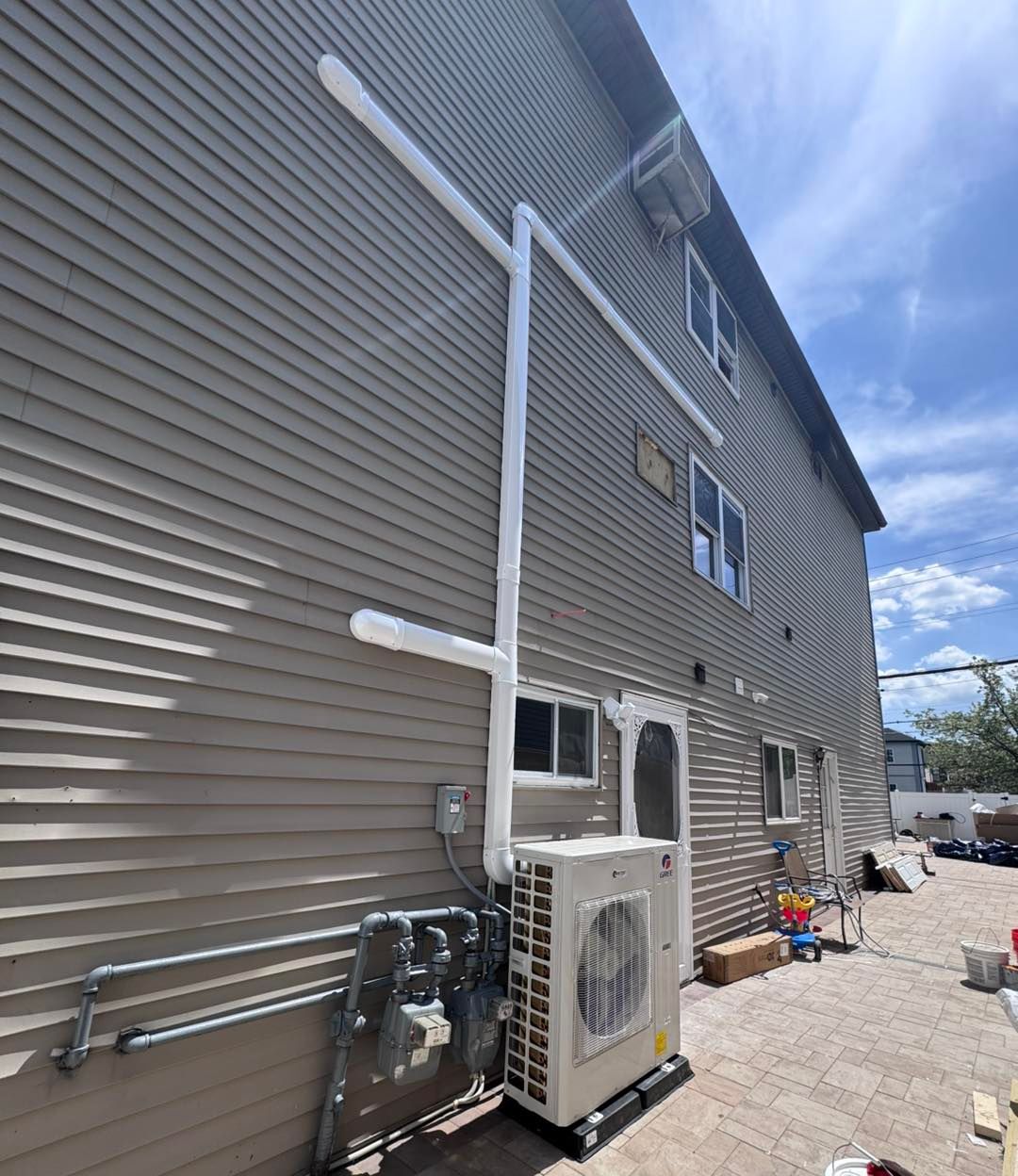 Exterior of a building with HVAC system installed; white pipes run along the wall.
