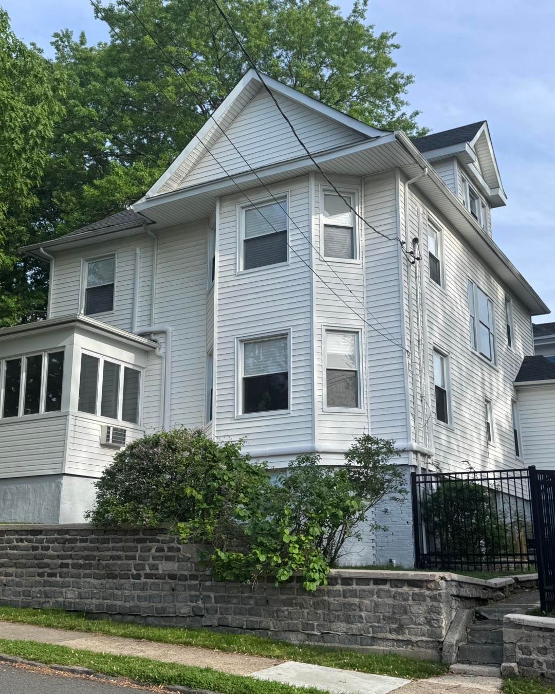 Two-story white house with bay windows and a brick retaining wall in front.
