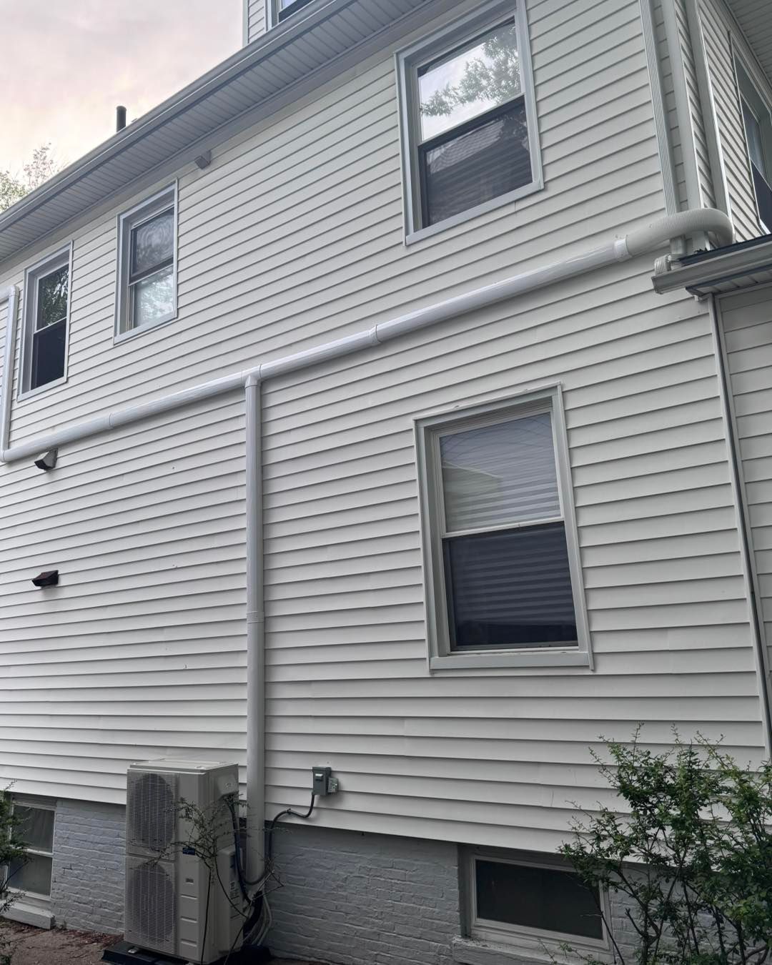 White house exterior with horizontal and vertical white pipes; air conditioning unit at the bottom.