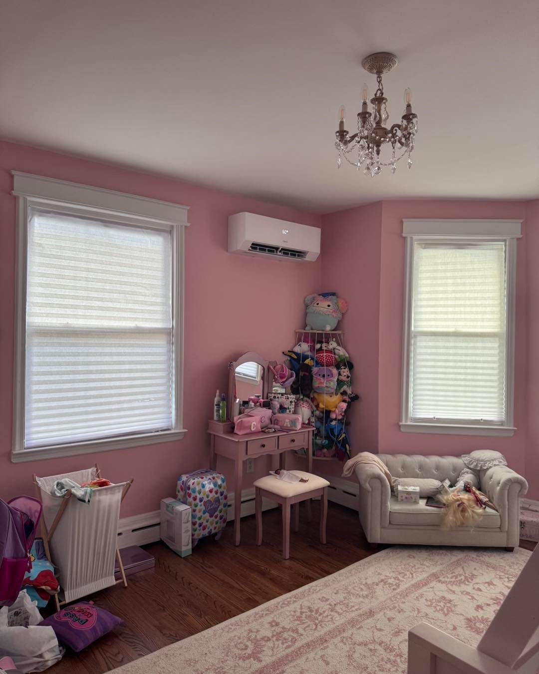 Pink bedroom with windows, a vanity, a small couch, and a chandelier. An air conditioning unit is on the wall.
