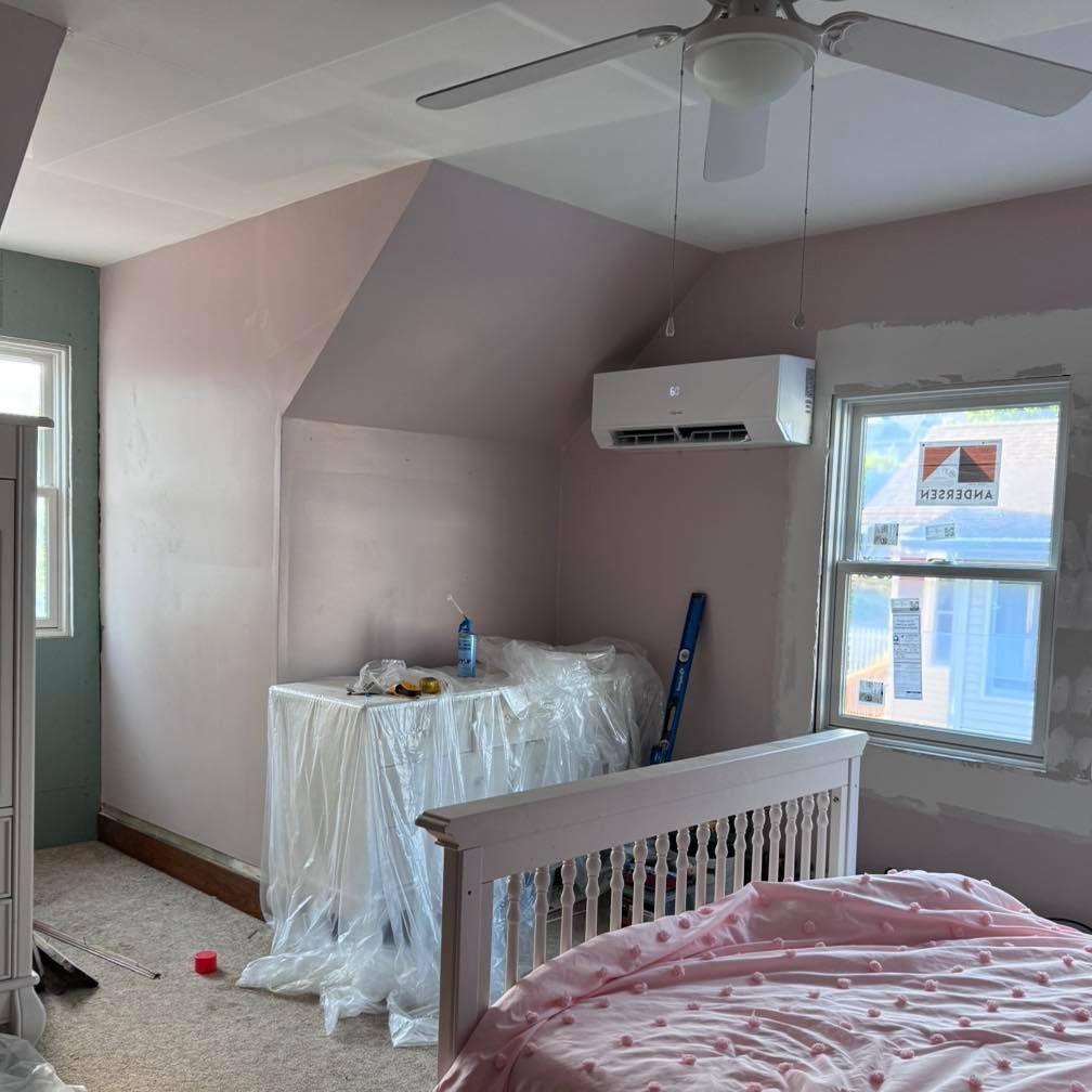 Bedroom with pink walls, an air conditioner, and a bed with a pink comforter. Construction materials are visible.