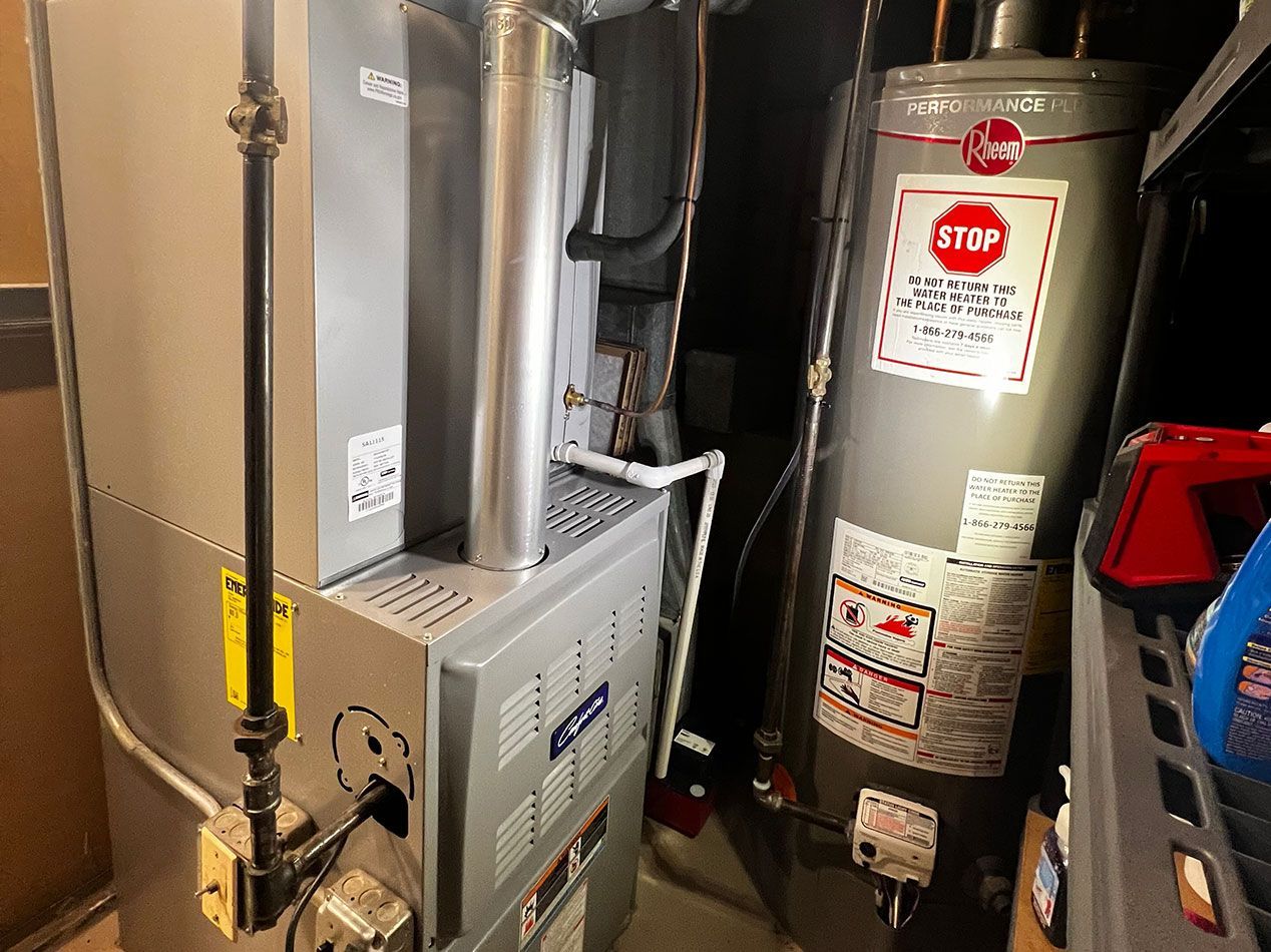 Furnace and water heater in a utility room. Gray metal units with a vent and plumbing.